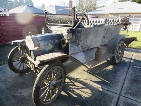 1912 Ford Model T - A weathered touring car sits in a driveway on a sunny day, with a dog visible behind a fence.