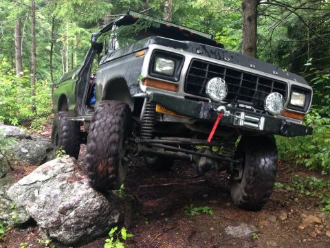 1979 Ford Bronco - Modified 1979 Ford Bronco navigating a challenging off-road course in a wooded area.