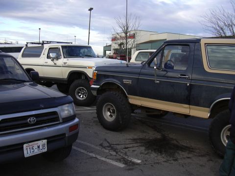 1991 Ford Bronco - A dark blue and tan 1991 Ford Bronco is parked next to a white Bronco and a Toyota SUV.
