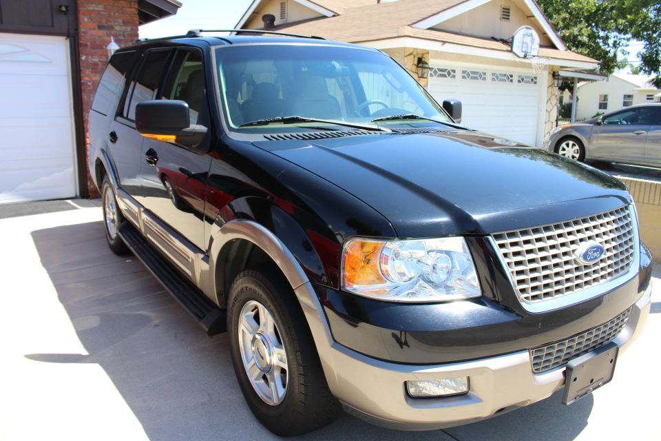 Black Ford Expedition parked in driveway, front quarter view. Another car is visible in the background