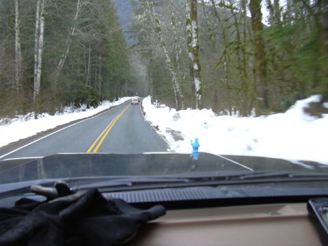1991 Ford Bronco - Driving on a snow-covered road through a forest with another vehicle visible ahead.
