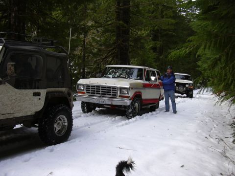 1991 Ford Bronco - Three off-road vehicles parked on a snow-covered forest road.