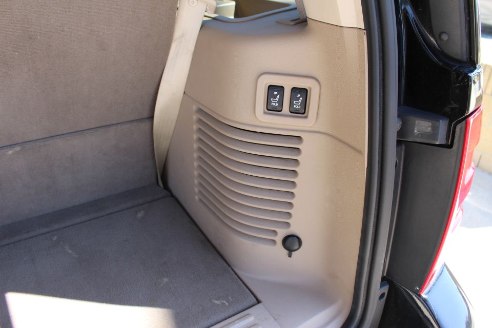 Interior cargo area of a 2003 Ford Expedition showing gray carpeted floor and seats, beige plastic trim with seat adjustment buttons, and a 12V power outlet