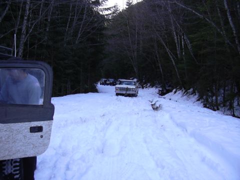 1991 Ford Bronco - A group of vehicles navigates a snowy path through a dense forest.