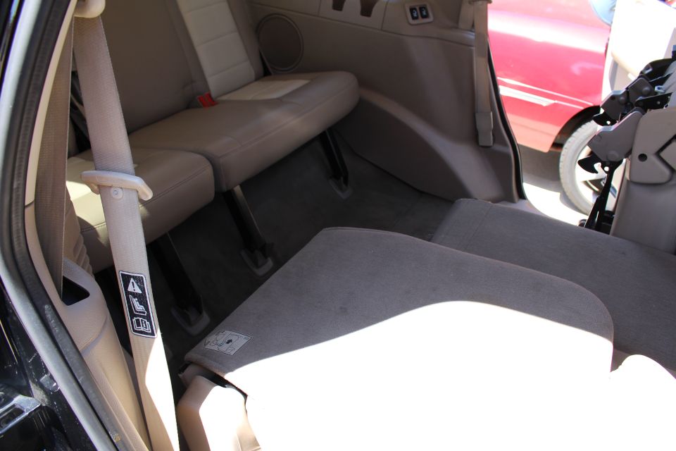 Tan interior of a 2003 Ford Expedition with folded seats, showing a seatbelt and a red car outside