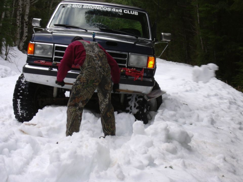 Dark blue 1991 Ford Bronco stuck in snow with "2 BIG BRONCOS 4x4 CLUB" sticker on windshield