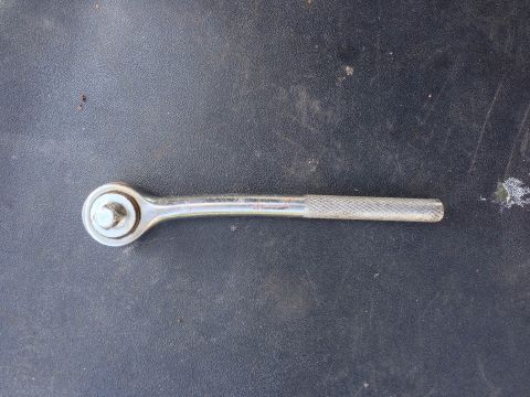 1979 Ford Bronco - A close-up view of a metal ratchet wrench lying on a textured dark surface.