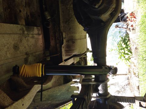 1979 Ford Bronco - Close-up of the undercarriage shows a shock absorber with a yellow protective boot mounted on the leaf spring suspension system.