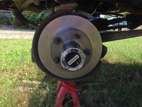 1979 Ford Bronco - A vehicle's wheel hub and brake rotor are shown, supported by a red jack stand on grassy ground.