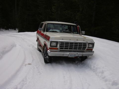 1991 Ford Bronco - A two-tone Ford Bronco drives on a snow-covered road through a forest.