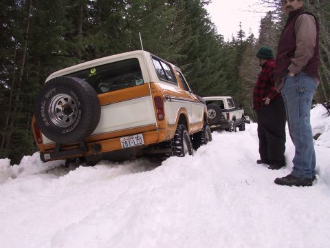 1991 Ford Bronco - Two vehicles navigate a snowy forest road, with one Bronco appearing to be stuck in deep snow.