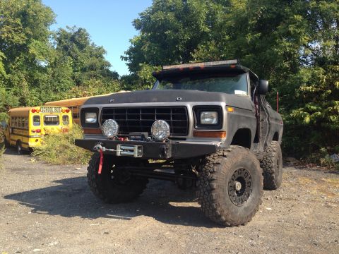 1979 Ford Bronco - Modified 1979 Ford Bronco with large off-road tires and winch parked next to a school bus.