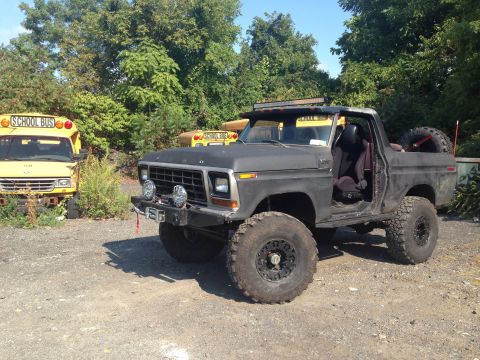 1979 Ford Bronco - A heavily modified Ford Bronco sits in a lot with several old school buses in the background.