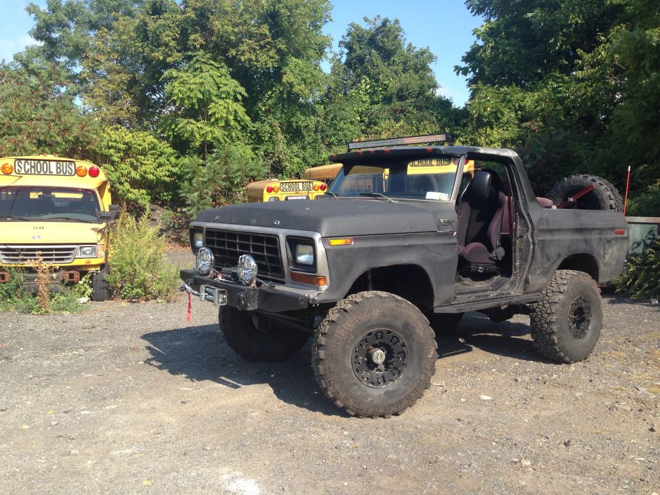 Black lifted Ford Bronco with off-road tires, parked next to yellow school buses