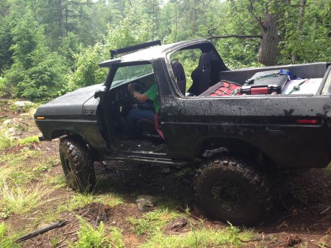 1979 Ford Bronco - A black 1978 Ford Bronco is shown off-road with its doors removed, navigating a muddy trail.