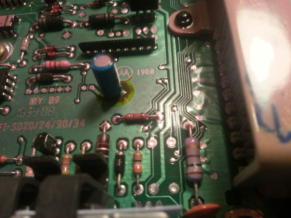 Close-up of a green circuit board with resistors, capacitors, and integrated circuits. Text reads 'MY 89' and '1988'