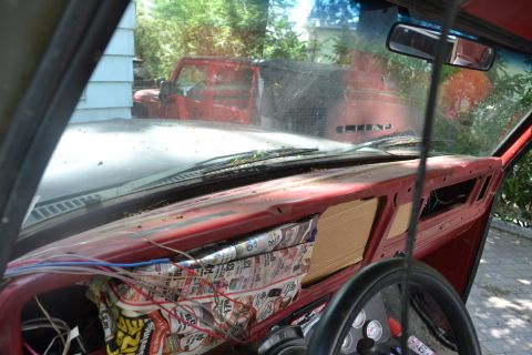 1979 Ford Bronco - The interior of a vehicle shows exposed wires and newspaper stuffing, with a red Jeep visible through the windshield.