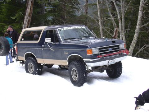 1991 Ford Bronco - Ford Bronco parked in a snowy wooded area with a spare tire on the back.