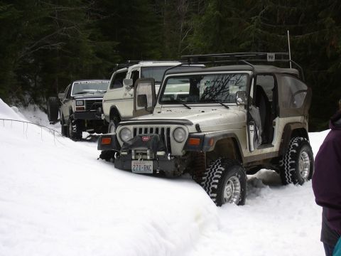 1991 Ford Bronco - Several off-road vehicles navigate a snow-covered trail in a wooded area.