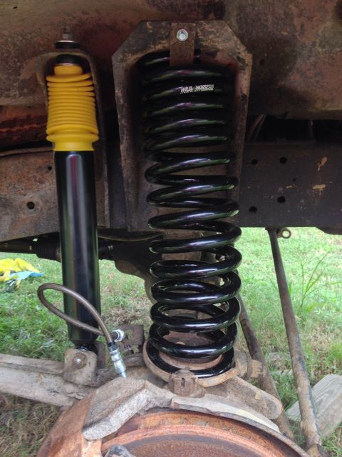 1979 Ford Bronco - Close-up of a new black coil spring and a yellow-capped shock absorber installed on a vehicle's front suspension.