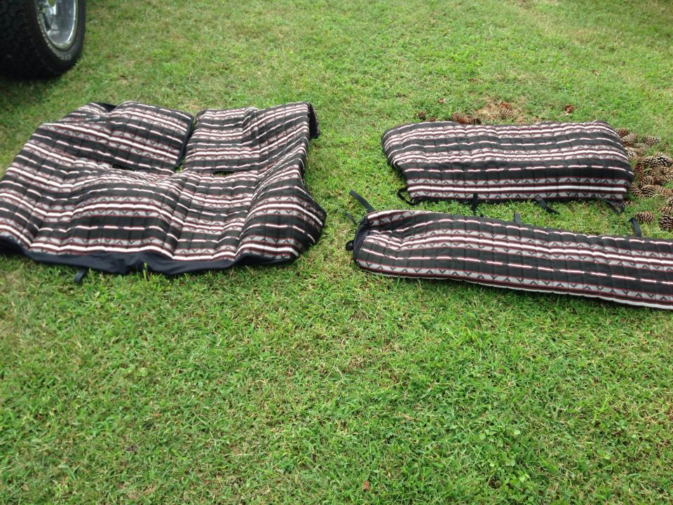 Car seat covers with a striped pattern laid out on grass. A tire and part of a vehicle are visible on the left