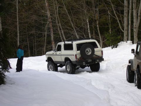 1991 Ford Bronco - A white Ford Bronco navigates a snowy path with trees in the background and another vehicle nearby.