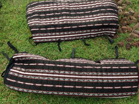 1979 Ford Bronco - Two seat covers with a black, white, and red striped pattern are laid out on the grass next to a pile of pine cones.