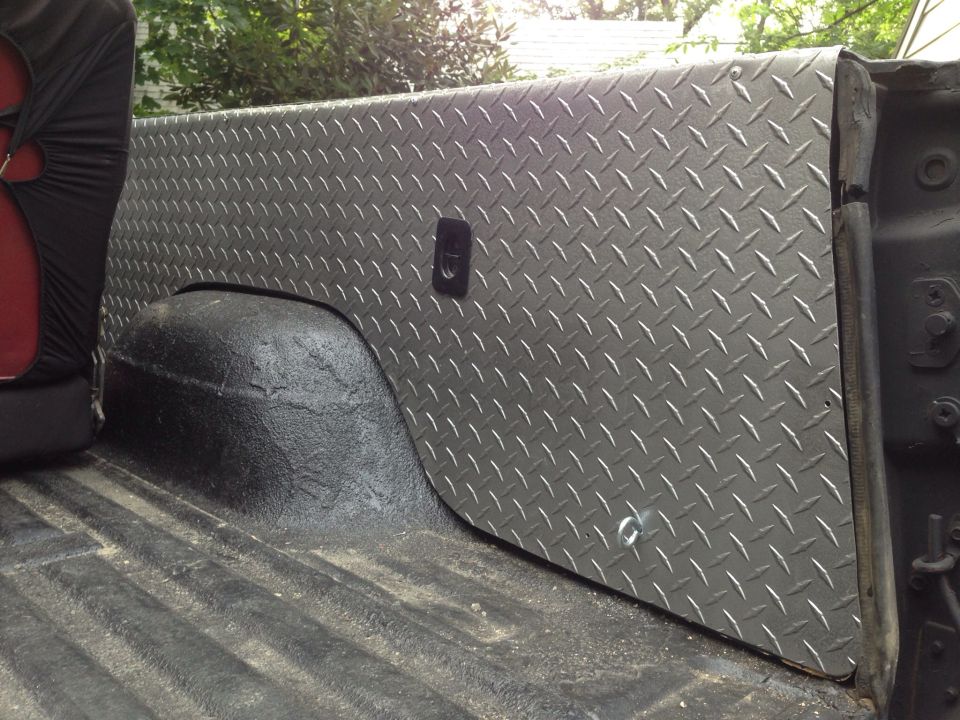 Diamond plate bed liner installed over the wheel well in a truck bed. Seat cover visible on left