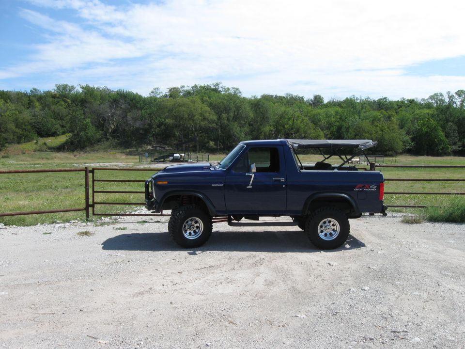 Blue Ford Bronco with soft top parked on gravel, side view. "4x4 OFF ROAD" decal visible