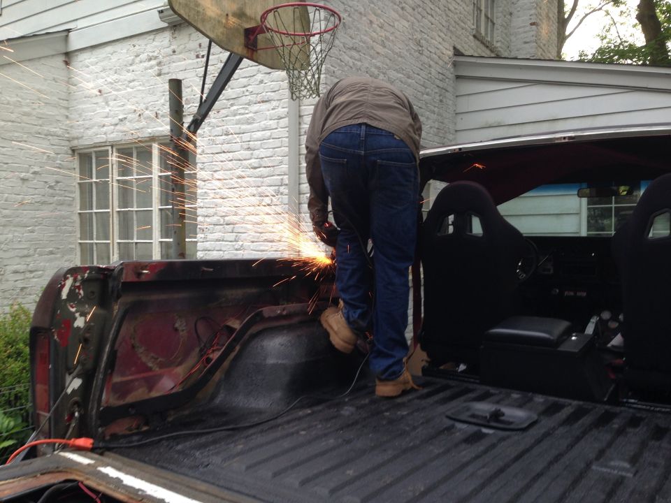 Person welding the rear of a red 1978 Ford Bronco with racing seats visible inside