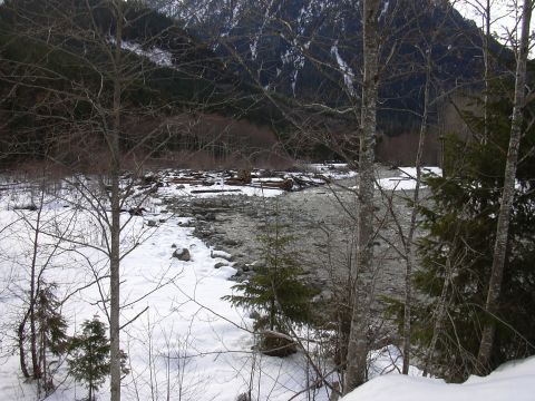 1991 Ford Bronco - A wide river flows through a snow-covered area, with trees and mountains visible in the distance.