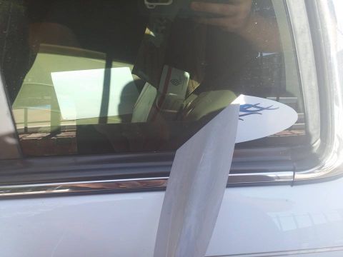 2000 Mercury Grand Marquis - A metallic object partially covers a sticker on the rear passenger window of a white car.