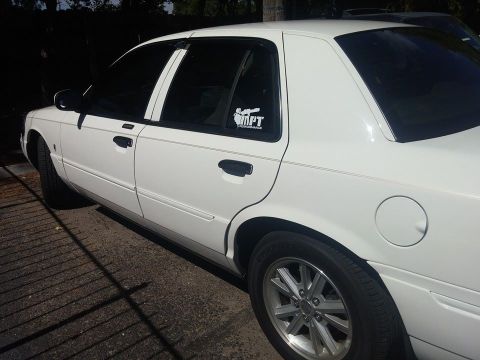 2000 Mercury Grand Marquis - White 2000 Mercury Grand Marquis sedan with aftermarket wheels and a sticker on the rear window.