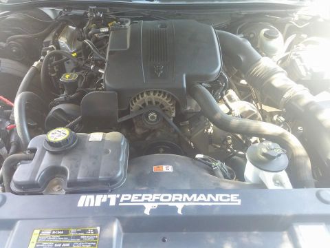 2000 Mercury Grand Marquis - The engine bay of a vehicle, a prominent black engine cover and various mechanical components.