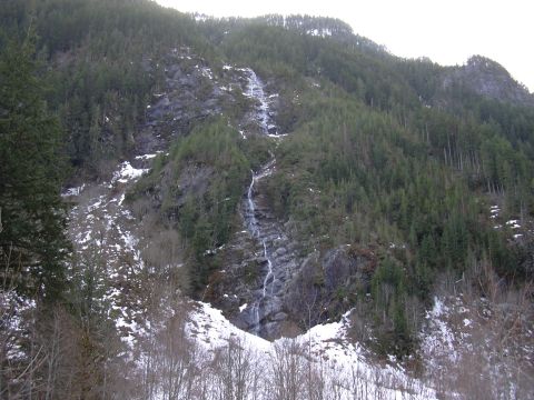 1991 Ford Bronco - A remote mountain scene with a waterfall flowing down a rocky slope, partially covered in snow and surrounded by dense forest.