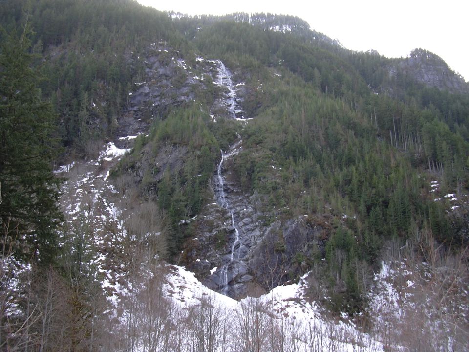 Waterfall cascading down a snow-dusted mountainside covered in evergreen trees