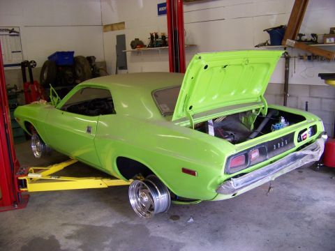 1974 Dodge Challenger - A lime green muscle car is being worked on in a garage, with its trunk open and wheels removed.