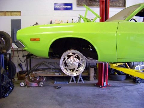 1974 Dodge Challenger - A lime green muscle car is up on a lift in a garage, showing its front suspension area.