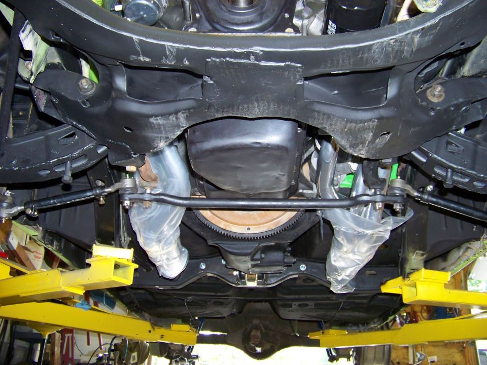 Underside view of a 1974 Dodge Challenger front suspension with steering linkage and exhaust pipes visible