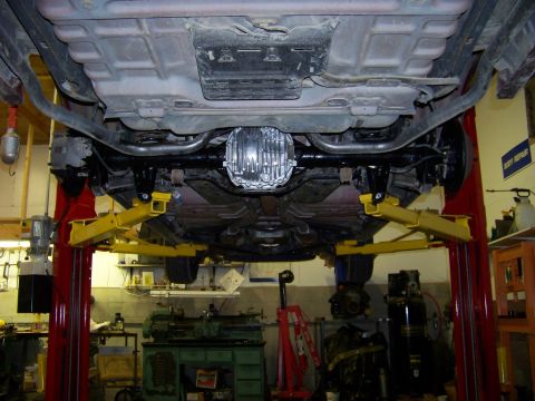 1999 Mercury Grand Marquis - The rear axle and exhaust system of a vehicle are visible while it's raised on a hydraulic lift in a workshop.