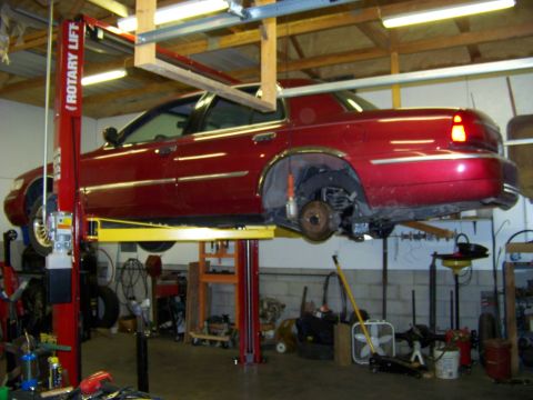 1999 Mercury Grand Marquis - A red 1999 Mercury Grand Marquis is raised on a car lift in a garage, undergoing service.