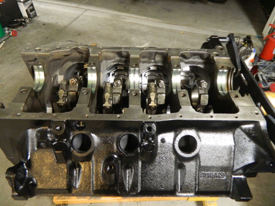 Engine block with crankshaft and connecting rods visible, black metal, on wooden supports