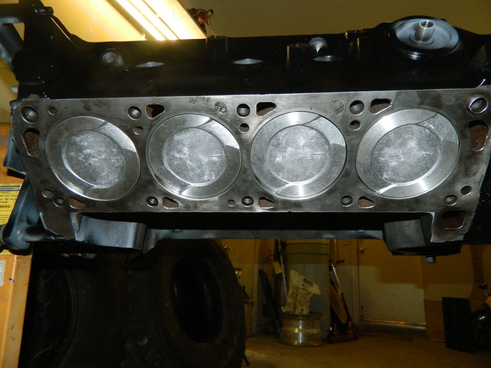 Engine block showing four pistons and cylinder bores. Part of an engine assembly is visible above