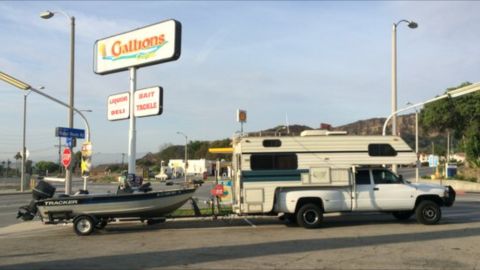 1997 Dodge 3500 - A white pickup truck tows a boat on a trailer past a gas station sign.