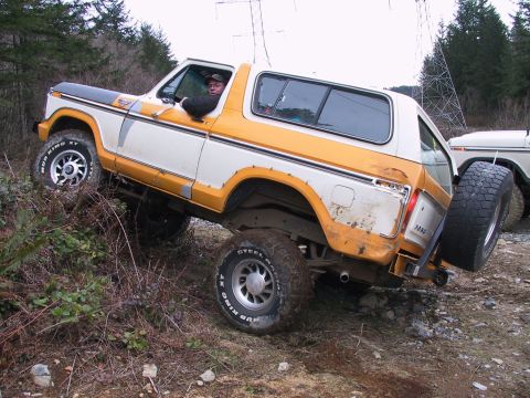 1991 Ford Bronco - A white and orange Ford Bronco is shown off-road, with a second vehicle partially visible behind it.