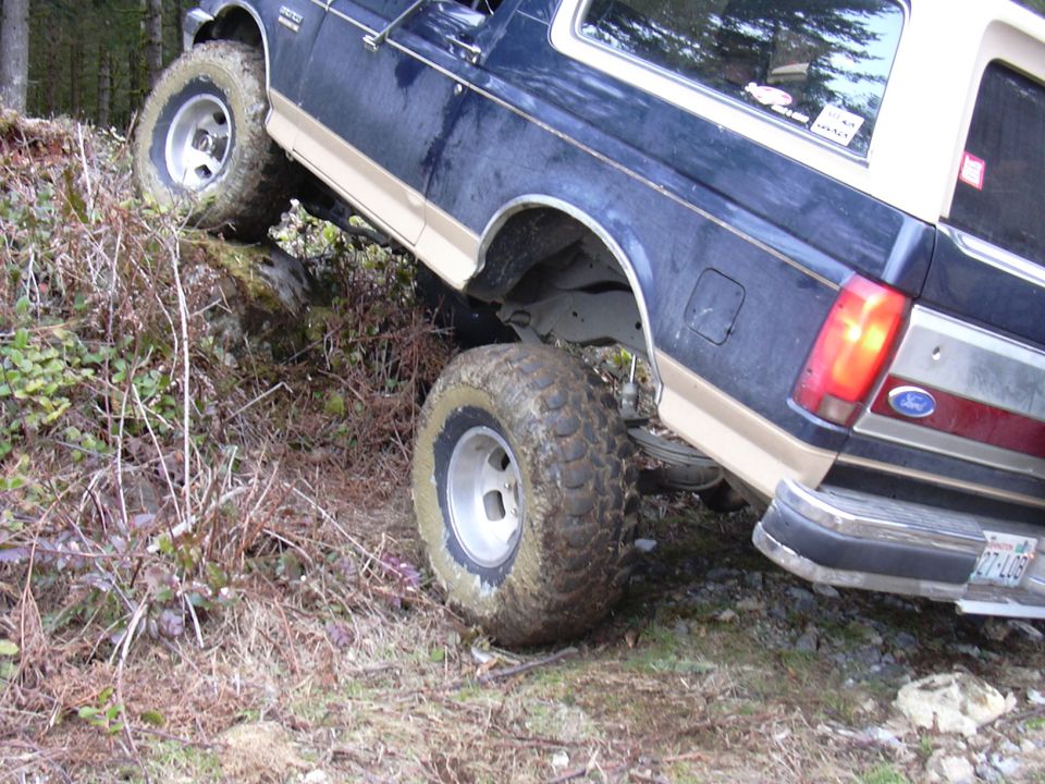 1991 Ford Bronco climbing a dirt hill, rear view showing mud-splattered tires and body