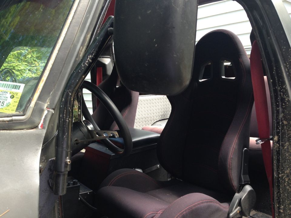 Interior of a vehicle with racing seats, roll cage, and a New York State inspection sticker on the windshield