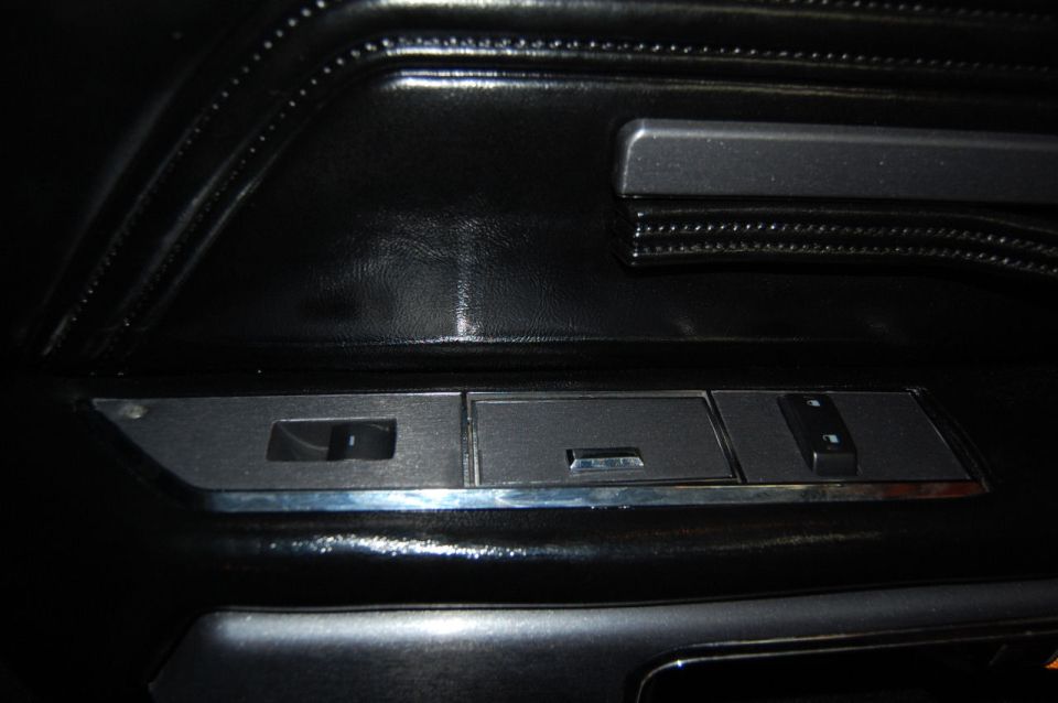 Close-up of a black car door panel with window controls and a chrome trim piece