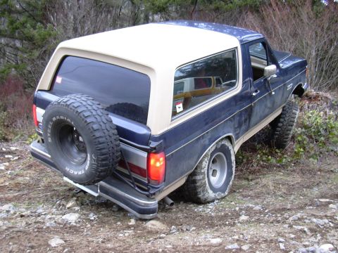 1991 Ford Bronco - This 1991 Ford Bronco is shown off-road on a dirt path with trees in the background.