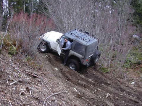 1991 Ford Bronco - A Jeep Wrangler navigates a challenging muddy slope, with a person exiting the vehicle.
